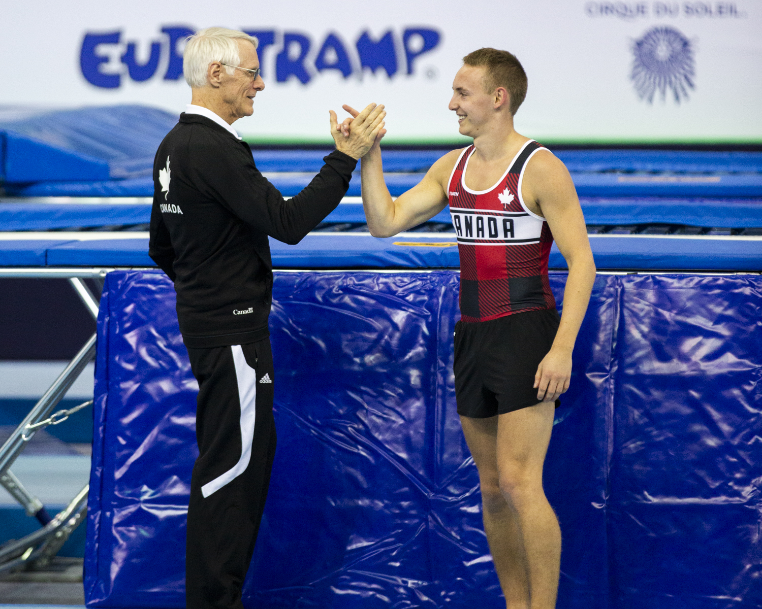 Photographie couleur du canadien Keegan Soehn serant la main de son entraineur heureux d'avoir terminé son passage en Trampoline