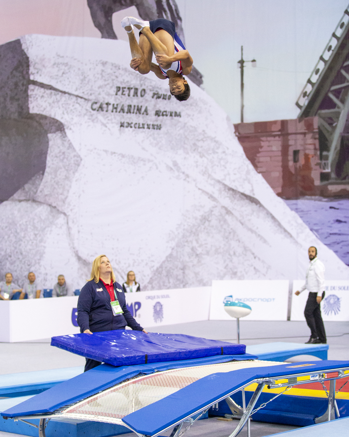 Photographie couleur de l'américain Ruben Padilla, vice champion du monde de double mini trampoline, en position de salto groupé sous l'oeil attentif de son entraineur