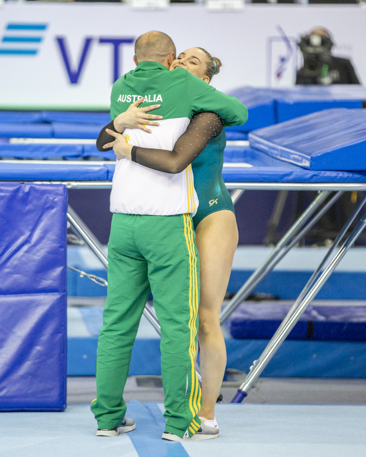 Photographie couleur de l'australienne Kira Ward enlaçant son entraineur heureuse après avoir terminé son passage au trampoline