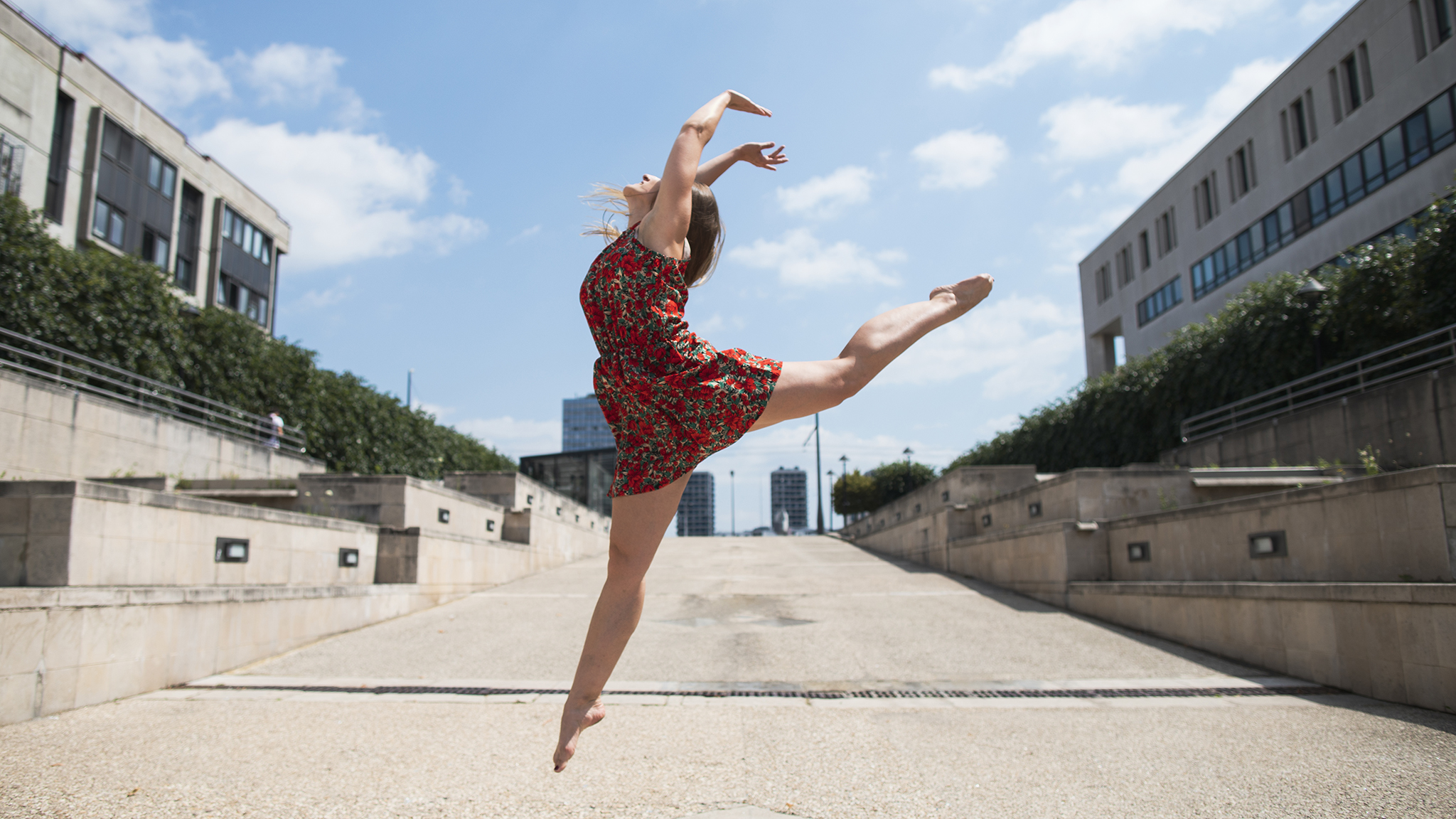 Photographie en couleur de Cécile Reiter qui fait un saut de danseuse au centre ville de Nancy dans des habits de tous les jours