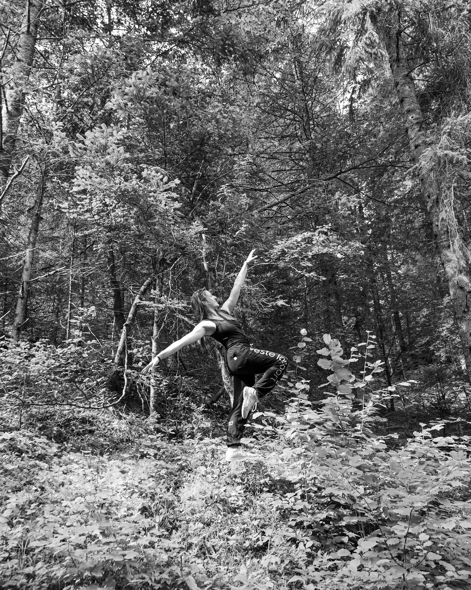Photographie en niveau de gris de Cécile Reiter qui prend la pose en dansant au milieu d'une forêt du Jura