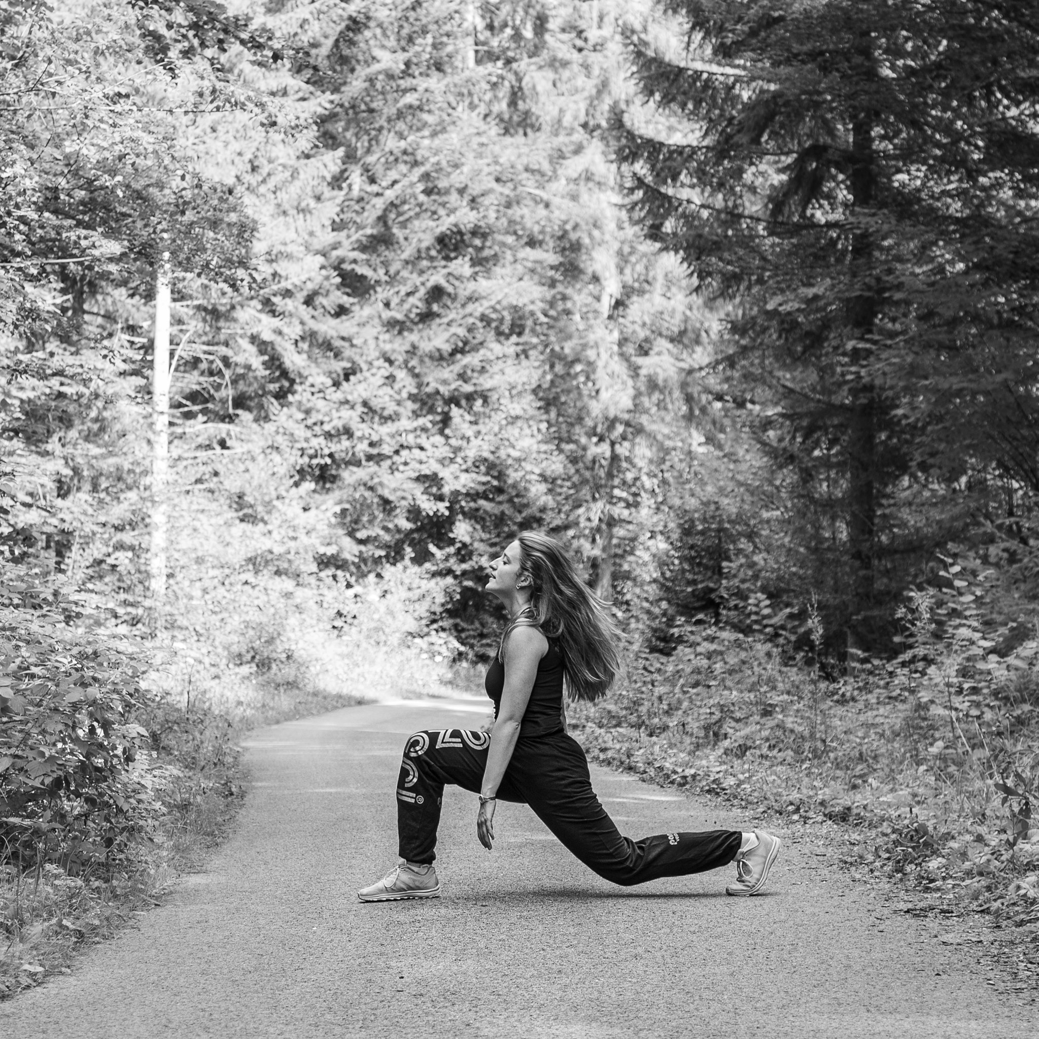 Photographie en niveau de gris de Cécile Reiter qui danse au milieu d'une route dans une forêt du Jura