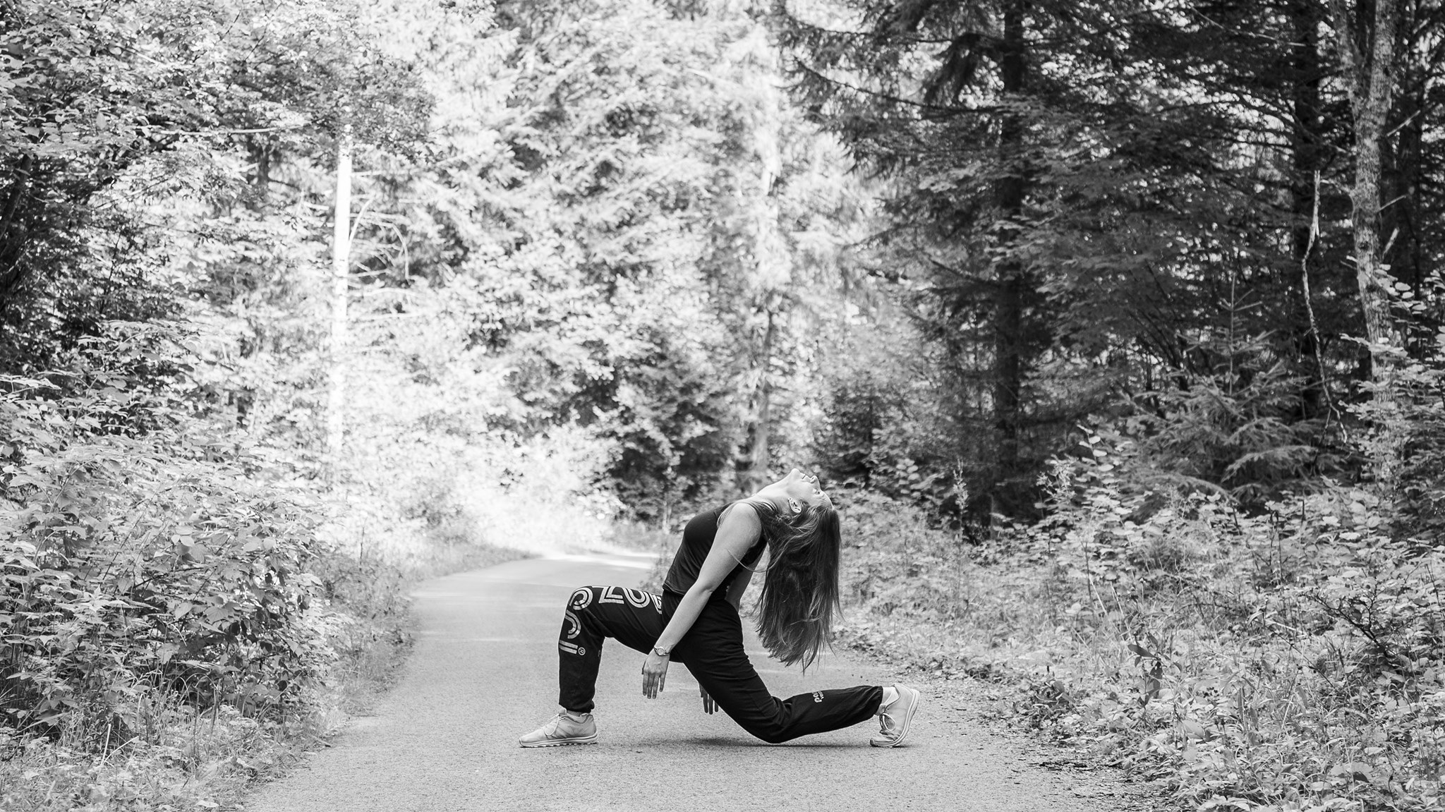 Photographie en niveau de gris de Cécile Reiter qui danse au milieu d'une route dans une forêt du Jura