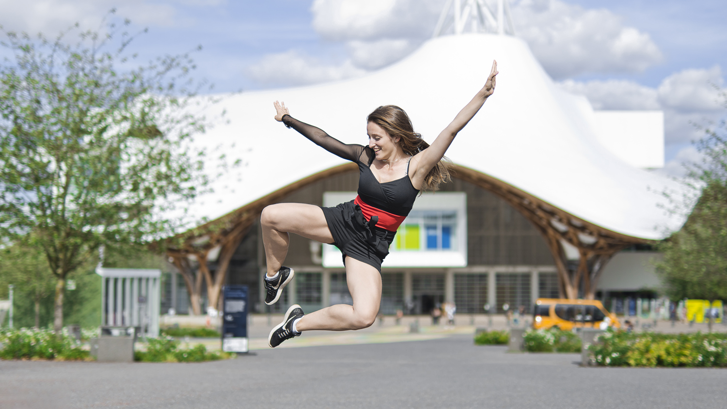 Photographie couleur de Cécile Reiter qui effectue un saut de danse nommé Aile de Pigeon devant le Centre Pompidou de Metz