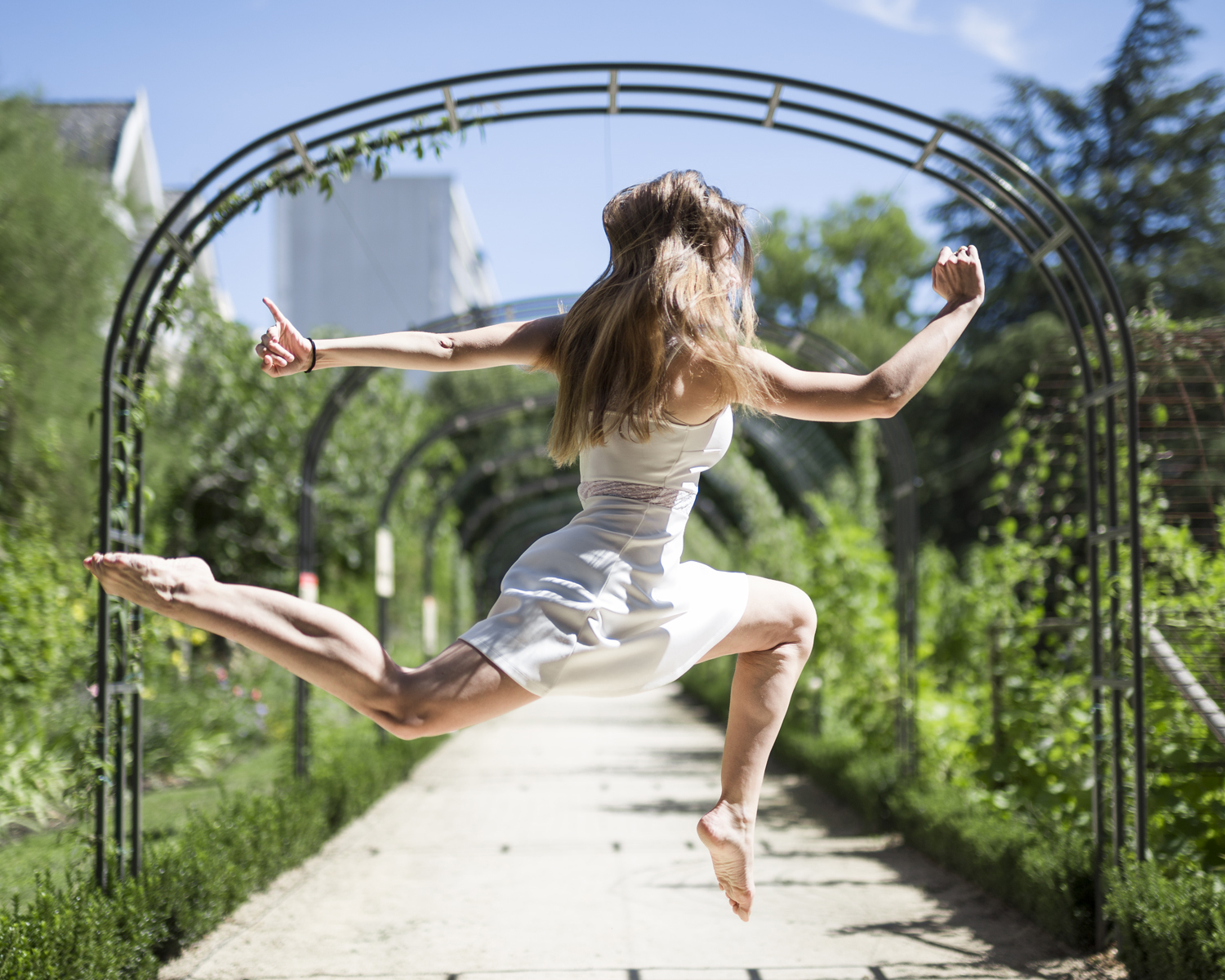 Photographie couleur de Cécile Reiter, danseuse, effectuant un saut écart en attitude dans le jardin botanique de Metz