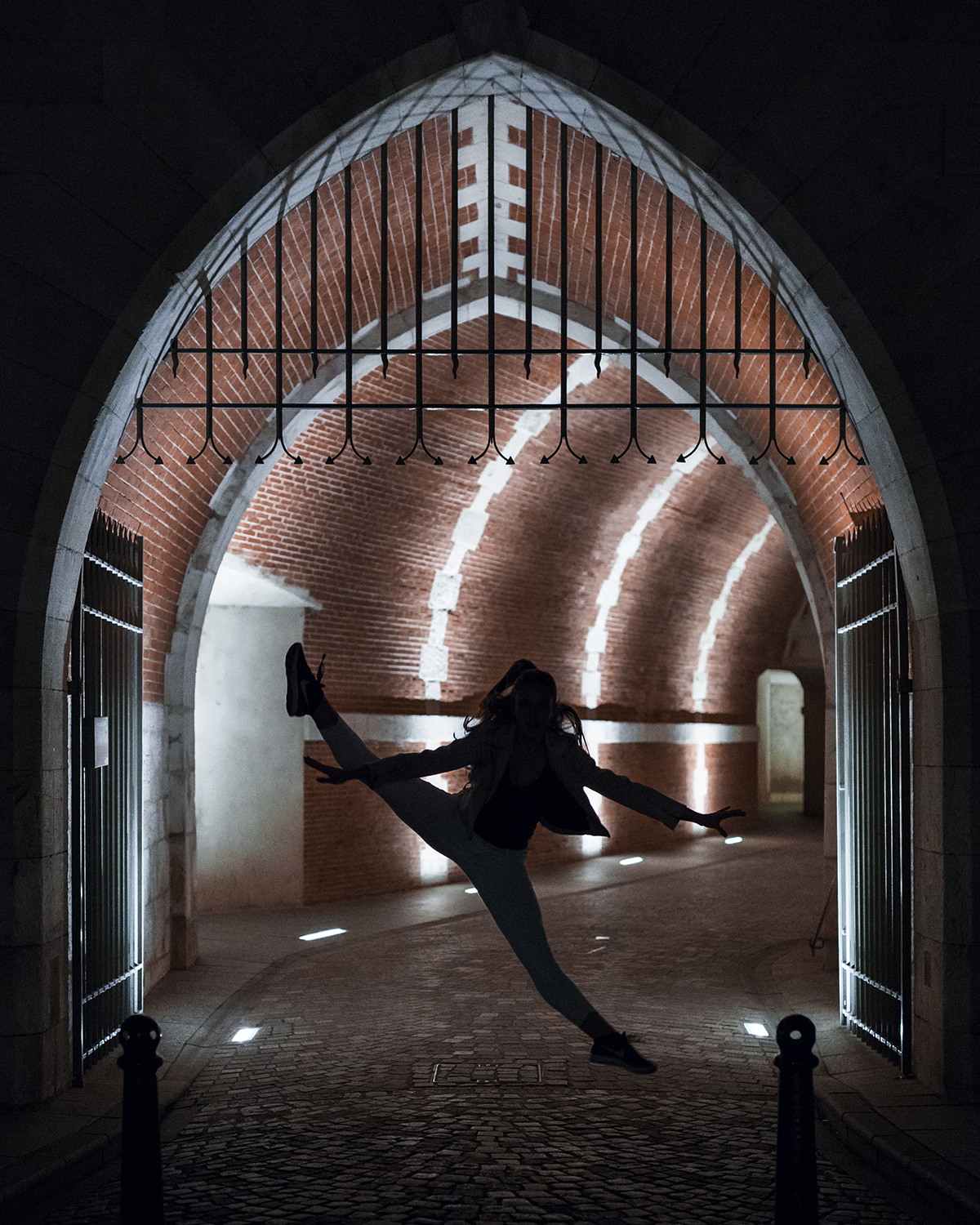 Photographie couleur de Cécile Reiter, danseuse, qui effectue un saut écart dans une ruelle sombre de Nancy et créé un contre-jour